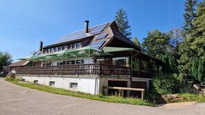 Ein Gebäude mit einem geneigten Dach, Solaranlagen und einem Balkon mit grünen Sonnenschirmen.