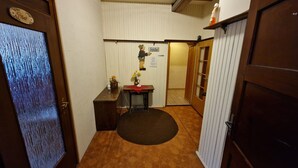 Ein schmaler Flur mit einer Holztür links, einem kleinen Tisch mit Blumenvase und einem Schild, das eine Toilette anzeigt.