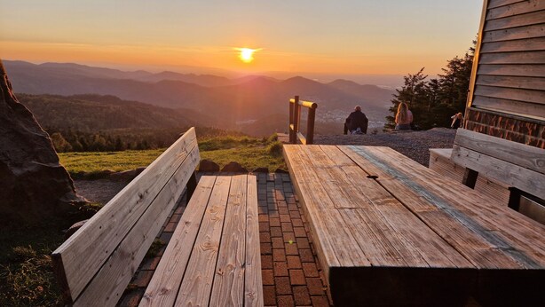 Ein Holztisch mit Bänken mit Blick auf eine Berglandschaft im Abendrot.