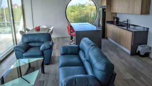 En moderne stue med sofa, sofabord i glas og et spiseområde med bord og stole.