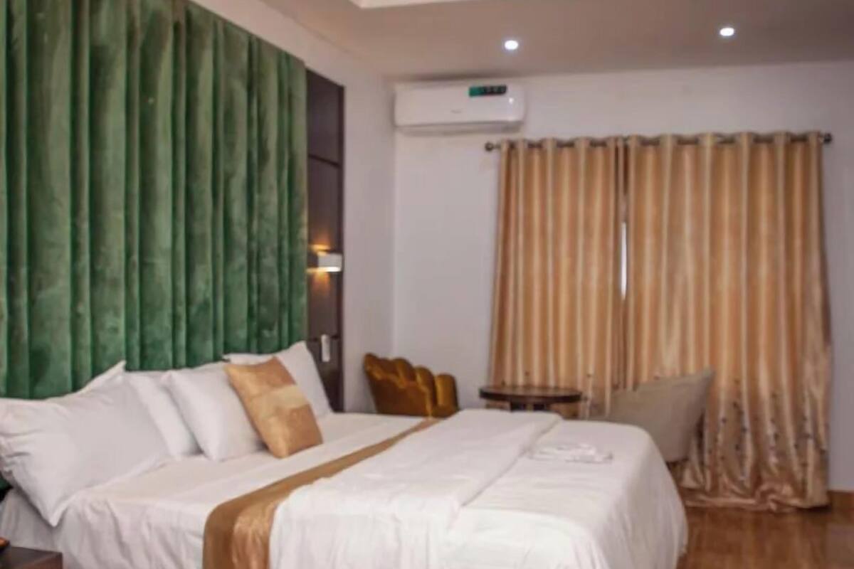 Une chambre d’hôtel avec un grand lit, une table de chevet, une petite table et un rideau vert.