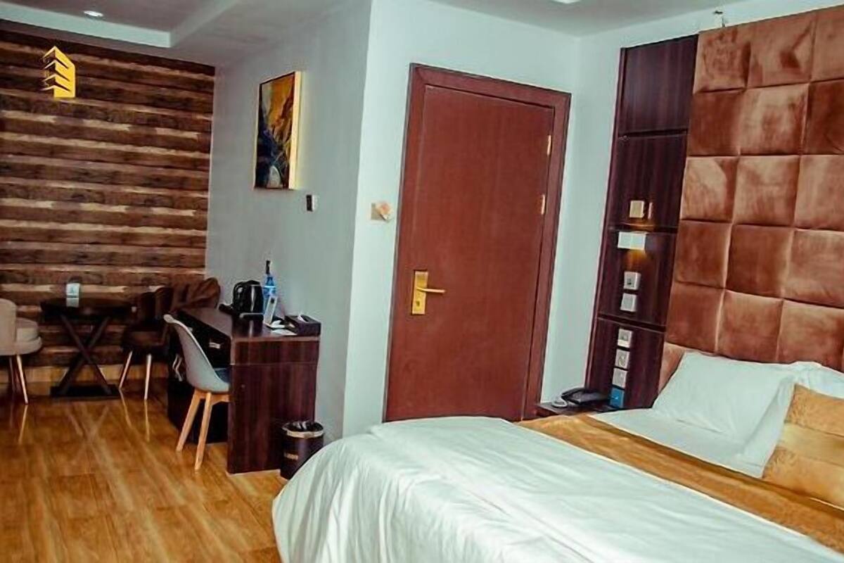 Une chambre d’hôtel avec un mur en bois, un lit avec une literie blanche, un bureau avec une chaise et une porte.