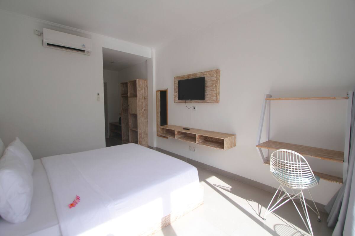 A bedroom with a bed, a TV mounted on the wall, a wooden shelf, and a chair.