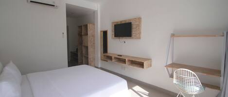 Un dormitorio con una cama, un televisor en la pared, un estante de madera y una silla.