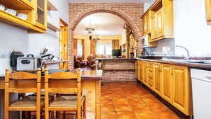 A kitchen with wooden cabinets, a brick archway, a dining area with chairs, and a tiled floor. - Villa Fuji Sierra de la Pandera (AN)