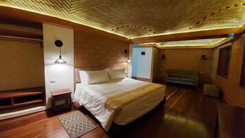A room with a brick-patterned ceiling, a bed with white bedding, a bench, a sofa, and a patterned rug.