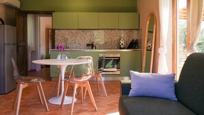 A modern kitchen with green cabinets, a white countertop, and a dining area with a white table and clear chairs. - La Leccina - Dependance (San Gimignano)