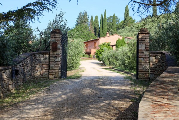 A gravel driveway leading to a rustic house with stone walls and a metal gate.