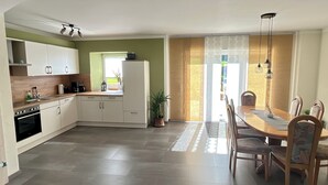A modern kitchen with white cabinets, a built-in oven, and a dining area with a wooden table and chairs. - Gemütliche Ferienwohnung mit Blick auf Wald Wiesen und Dolomiten (Gerolstein)