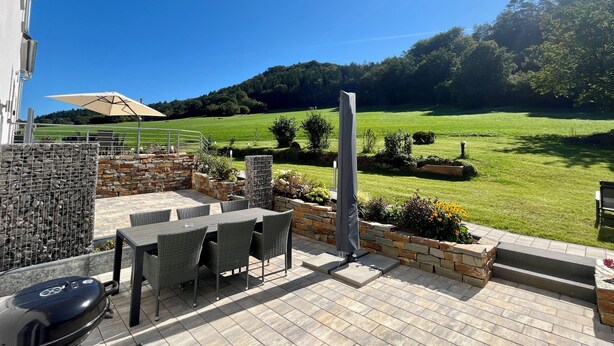 An outdoor patio with a table and chairs, a barbecue grill, and a view of a green field and trees. - Gemütliche Ferienwohnung mit Blick auf Wald Wiesen und Dolomiten (Gerolstein)
