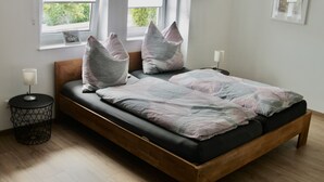 A modern bedroom with a wooden bed, a bedside table with a lamp, and a window with a view of greenery. - Gemütliche Ferienwohnung mit Blick auf Wald Wiesen und Dolomiten (Gerolstein)