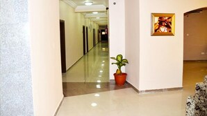 A hotel corridor with a potted plant, a framed picture on the wall, and a patterned chair. - Fox Premium Hotel Jos  (Jos)