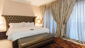 A hotel room with a large bed, a headboard, a bedside table, and a window with curtains. - Fox Premium Hotel Jos  (Jos)