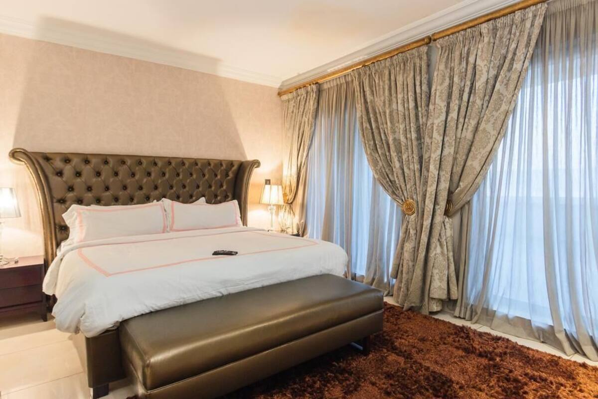 A hotel room with a large bed, a headboard, a bedside table, and a window with curtains.