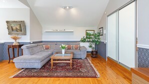 Ein Wohnzimmer mit einem grauen Ecksofa, einem Holztisch, einem Teppich mit rotem Muster und einer Topfpflanze.