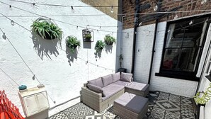 A patio with a wicker sofa, potted plants, and patterned tiles. - Rockton House (Whitby)