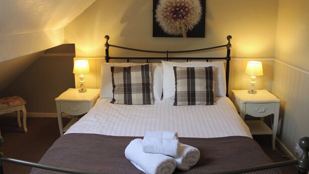 A neatly made bed with plaid pillows, two bedside lamps, and a dandelion artwork on the wall. - Rockton House (Whitby)