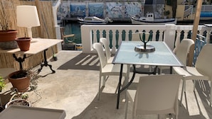 Eine Terrasse mit Tisch und Stühlen, Blumentöpfen und Blick auf Boote sowie eine Wand mit Graffiti.