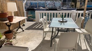 Una terrazza con tavolo e sedie, piante in vaso e vista su barche e un muro con graffiti.