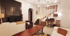A living room with a TV, sofa, wooden coffee table, and a staircase leading to a bedroom.