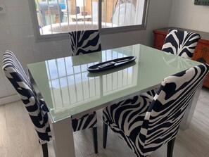A dining area with a glass-top table, zebra-patterned chairs, and a remote control on the table.