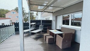 Un patio couvert comprenant une table et des chaises, un canapé en osier et une petite table sur laquelle est posé un saladier.