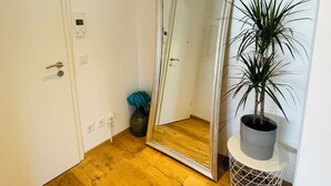 Une pièce avec un plancher en bois, un grand miroir, une plante en pot et une porte dotée d’une poignée.