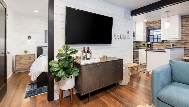 Un salon moderne avec un téléviseur à écran plat, un meuble en bois foncé, une plante en pot et un fauteuil bleu.