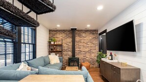 Un salon moderne avec un mur en briques, un grand téléviseur à écran plat, un canapé, une table basse en bois et une cheminée.