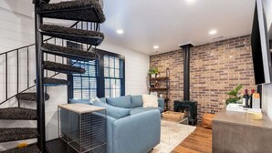 Un salon moderne avec un canapé bleu, un escalier en colimaçon et un mur en briques.