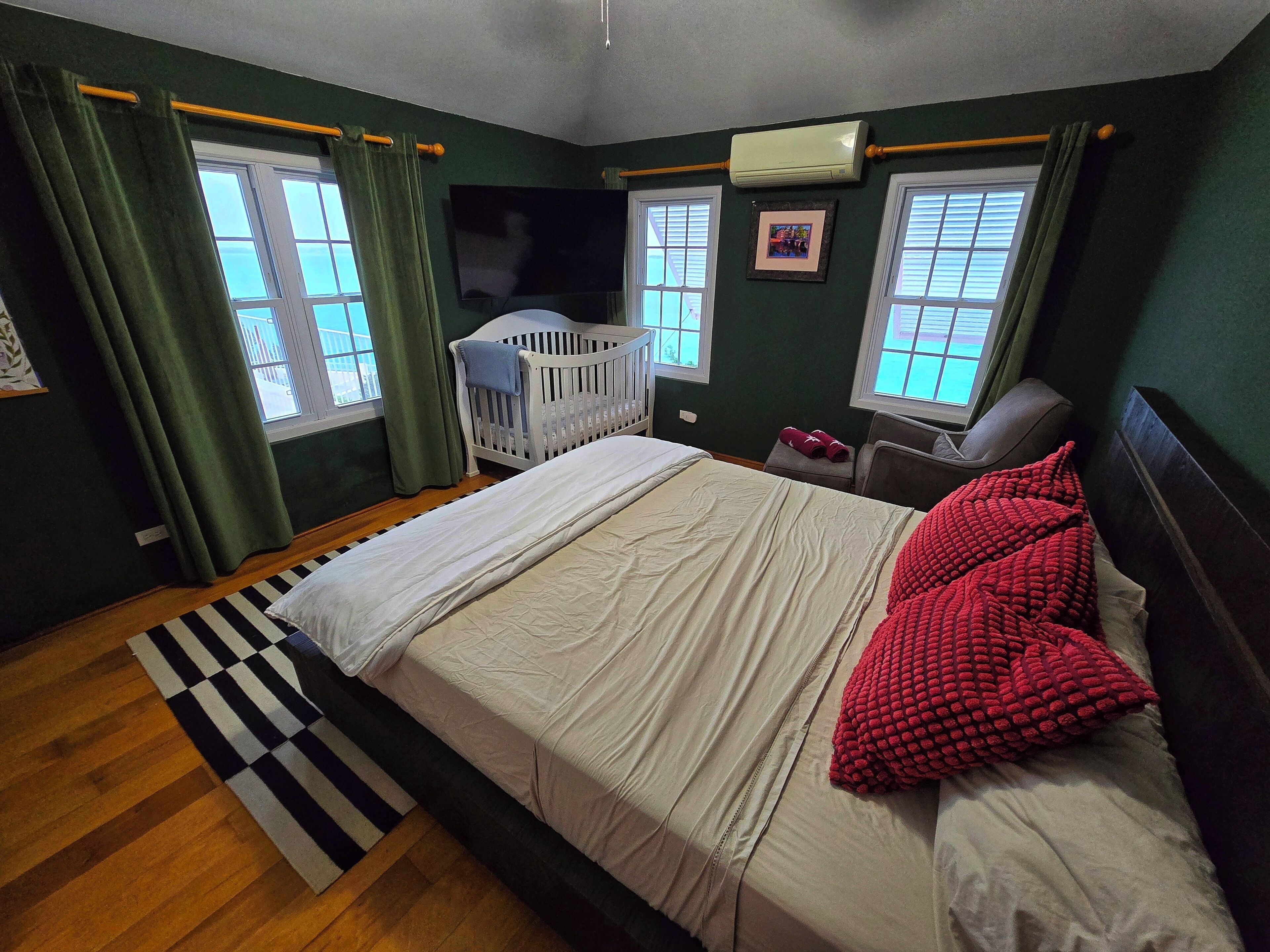Un dormitorio con una cama, una cuna, una ventana y un aire acondicionado de pared.