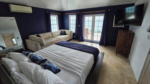 Un dormitorio con cama, sofá, televisor y balcón con vistas.