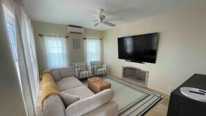 Una sala de estar con un sofá, sillones, un televisor de pantalla plana, una chimenea y un ventilador de techo.