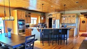 A modern kitchen with wooden cabinets, stainless steel appliances, and a central island with bar stools. - Mountain of Joy, 21-ZONE3029 (Estes Park)