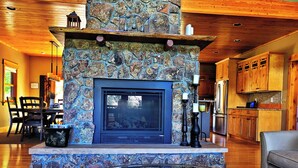 A stone fireplace with a glass door, surrounded by wooden cabinets and a dining area with chairs and a table. - Mountain of Joy, 21-ZONE3029 (Estes Park)