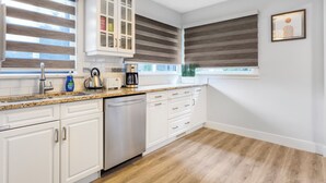 A modern kitchen with white cabinetry, a stainless steel dishwasher, a coffee maker, and a window with blinds. - Urban Nest 7 mins from Edmonton downtown <br> (Edmonton)