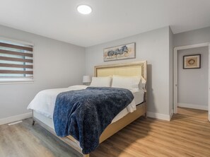 A neatly made bed with a blue blanket, a bedside lamp, and a framed picture on the wall. - Urban Nest 7 mins from Edmonton downtown <br> (Edmonton)