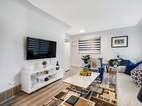 A modern living room with a flat-screen TV, white entertainment unit, and a coffee table with decorative items. - Urban Nest 7 mins from Edmonton downtown <br> (Edmonton)