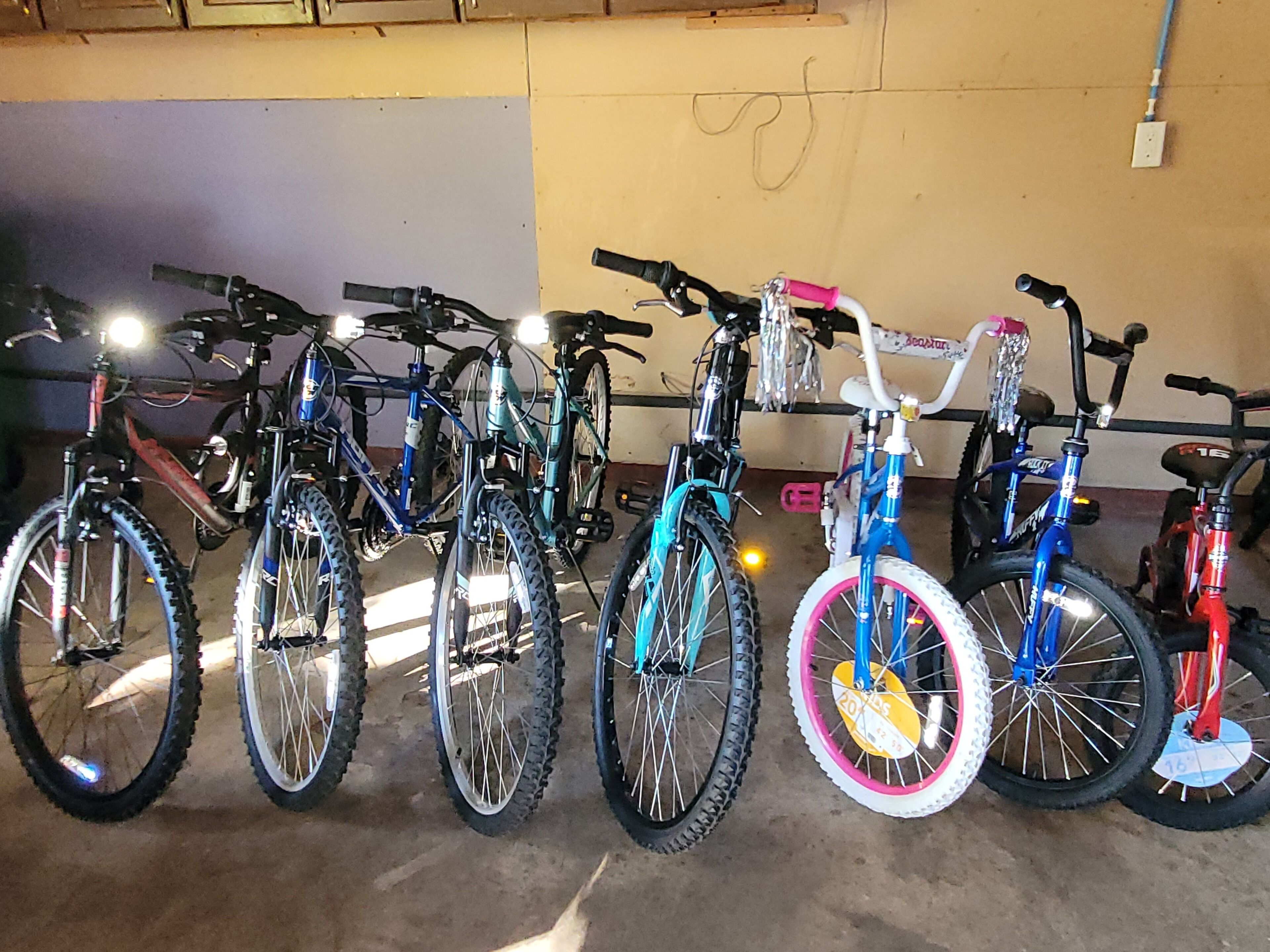 Bicycles parked in a garage with a concrete floor and a wooden door in the background.