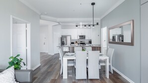 Una cucina moderna con mobili bianchi, un'isola centrale e un'area da pranzo con sedie bianche.