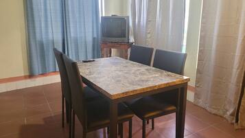 Una mesa de comedor con cuatro sillas, un televisor sobre un mueble bajo y cortinas.