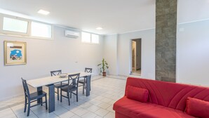Una sala de estar moderna con un sofá rojo, una mesa de comedor con sillas, una planta en maceta y un cuadro en la pared.