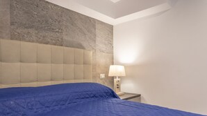 Una habitación de hotel con una cama grande, cabecera, mesita de noche y lámpara.