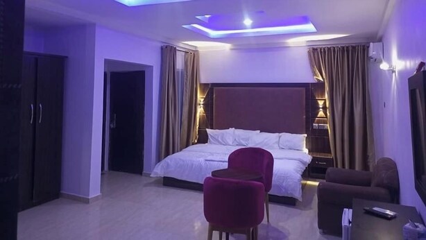 Una habitación de hotel moderna con una cama grande, una silla roja, una mesita pequeña y un televisor.