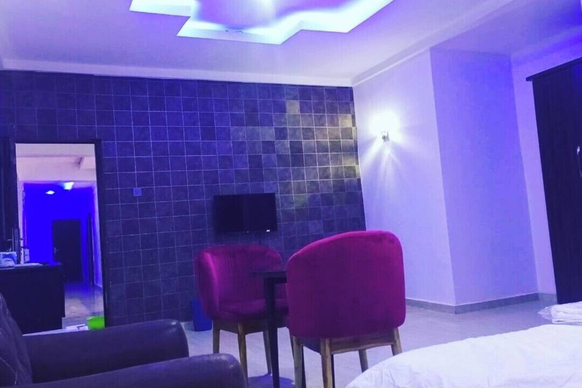 Ein modernes Hotelzimmer mit einer Wand in Fliesenoptik, einem flachbildfernseher über einem Holztisch und einem Bett mit weißer Bettwäsche.