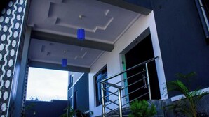 Una entrada moderna a un edificio con escaleras, barandales metálicos y una lámpara colgante azul.