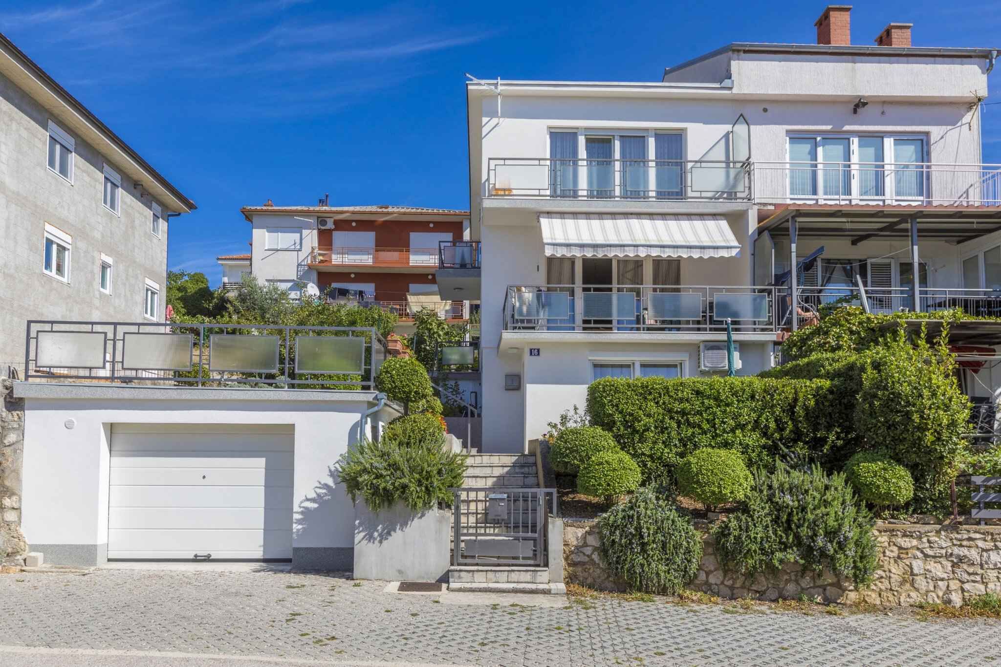 A residential building with a garage, a balcony, and a staircase leading to the upper floor.