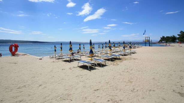 Ein Strand mit Reihen von Liegestühlen und Sonnenschirmen, einem Rettungsturm und einem strahlend blauen Himmel.