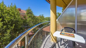 Ein Balkon mit einem weißen Tisch und einer Auswahl an Snacks, umgeben von Grünpflanzen und blauem Himmel.