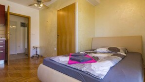Ein Schlafzimmer mit Bett, Holzboden, Deckenventilator und einer Tür zu einem anderen Raum.